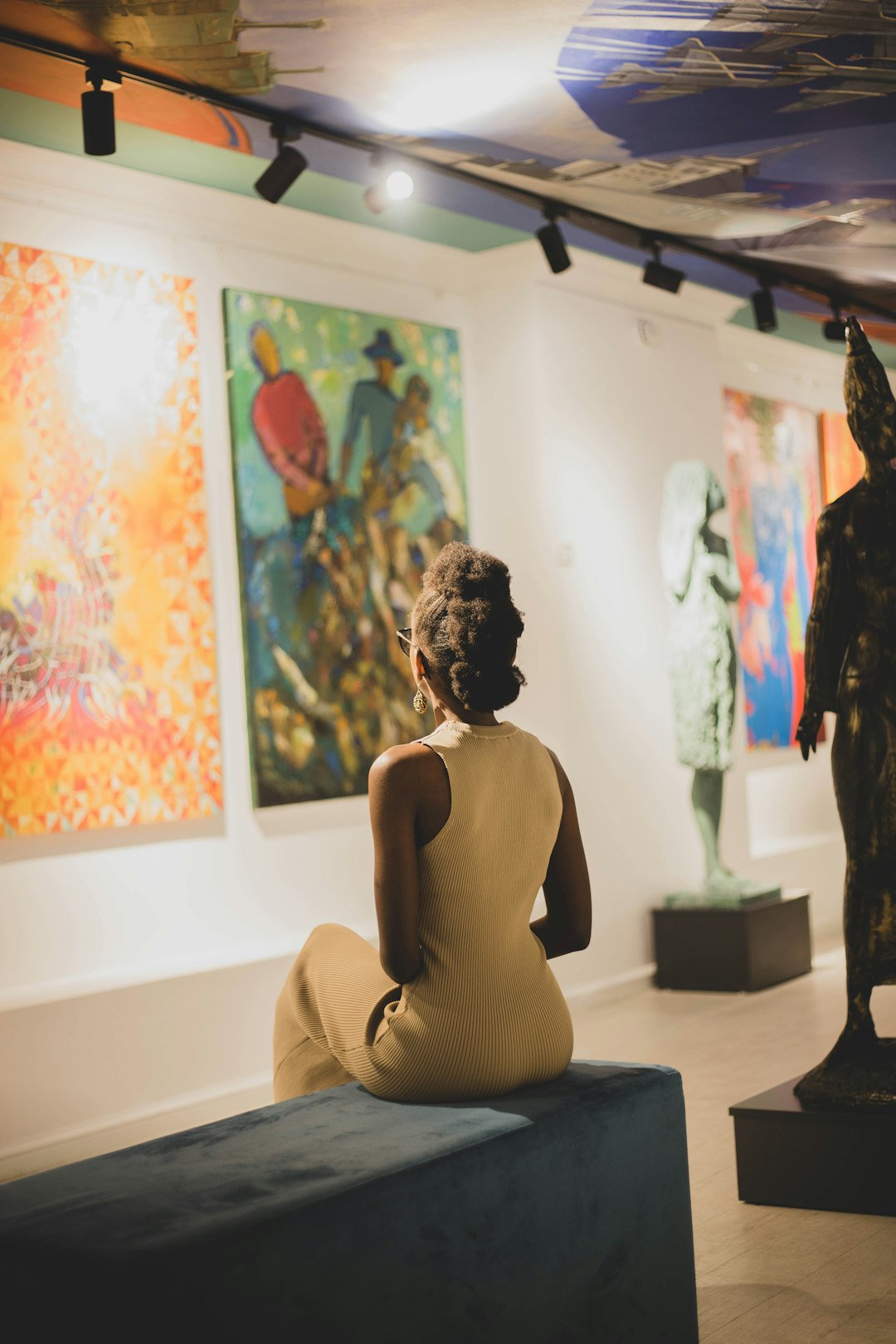 a-statue-of-a-person-sitting-on-a-couch-in-front-of-a-wall-of-paintings-45kg3p7u3qc