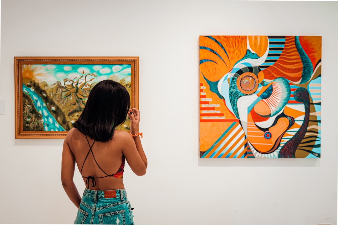 a-woman-standing-in-front-of-two-paintings-3cdjyesycga